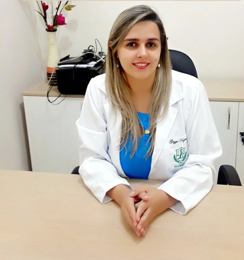 Geyza Nogueira de jaleco, sentada à mesa do consultório